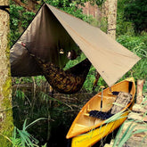 Bushmen ZEN Hammock setup near water with a kayak, ideal for lightweight camping and outdoor relaxation.
